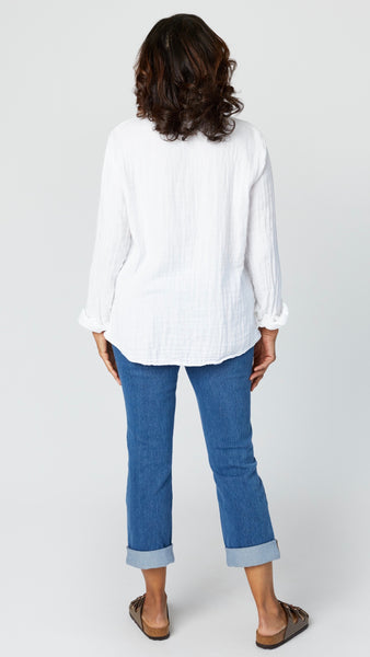Rear view of model wearing white double cotton button up shirt with cropped midwash jeans, and brown leather sandals.