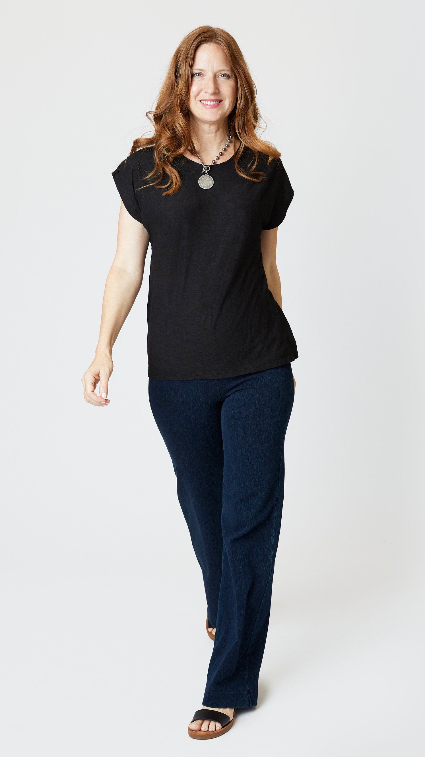 Model wearing black cotton-linen jersey top with cropped sleeves, boatneck, and boxy silhouette with indigo bootcut jeans, and sandals.