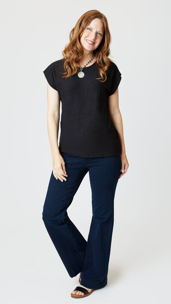 Model wearing black cotton-linen jersey top with cropped sleeves, boatneck, and boxy silhouette with indigo bootcut jeans, and sandals. 