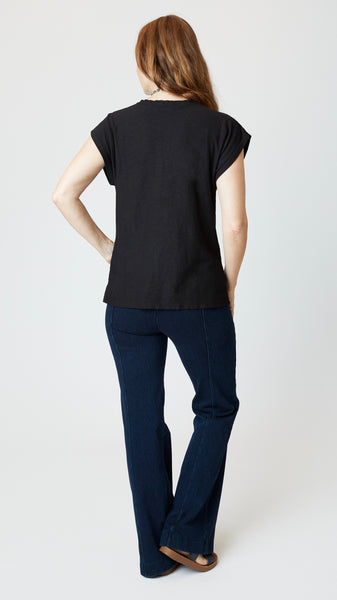 Model wearing black cotton-linen jersey top with cropped sleeves, boatneck, and boxy silhouette with indigo bootcut jeans, and sandals.