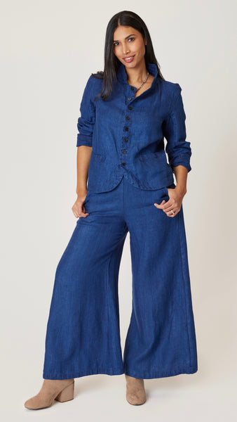 Model wearing indigo twill button front blazer jacket with rounded hem and standing collar, with indigo twill wide-leg pants.
