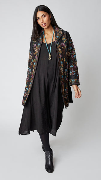 Model wearing black silk duster embroidered in dusty blue, purple, and brown tones over black rayon romper and black suede boots.