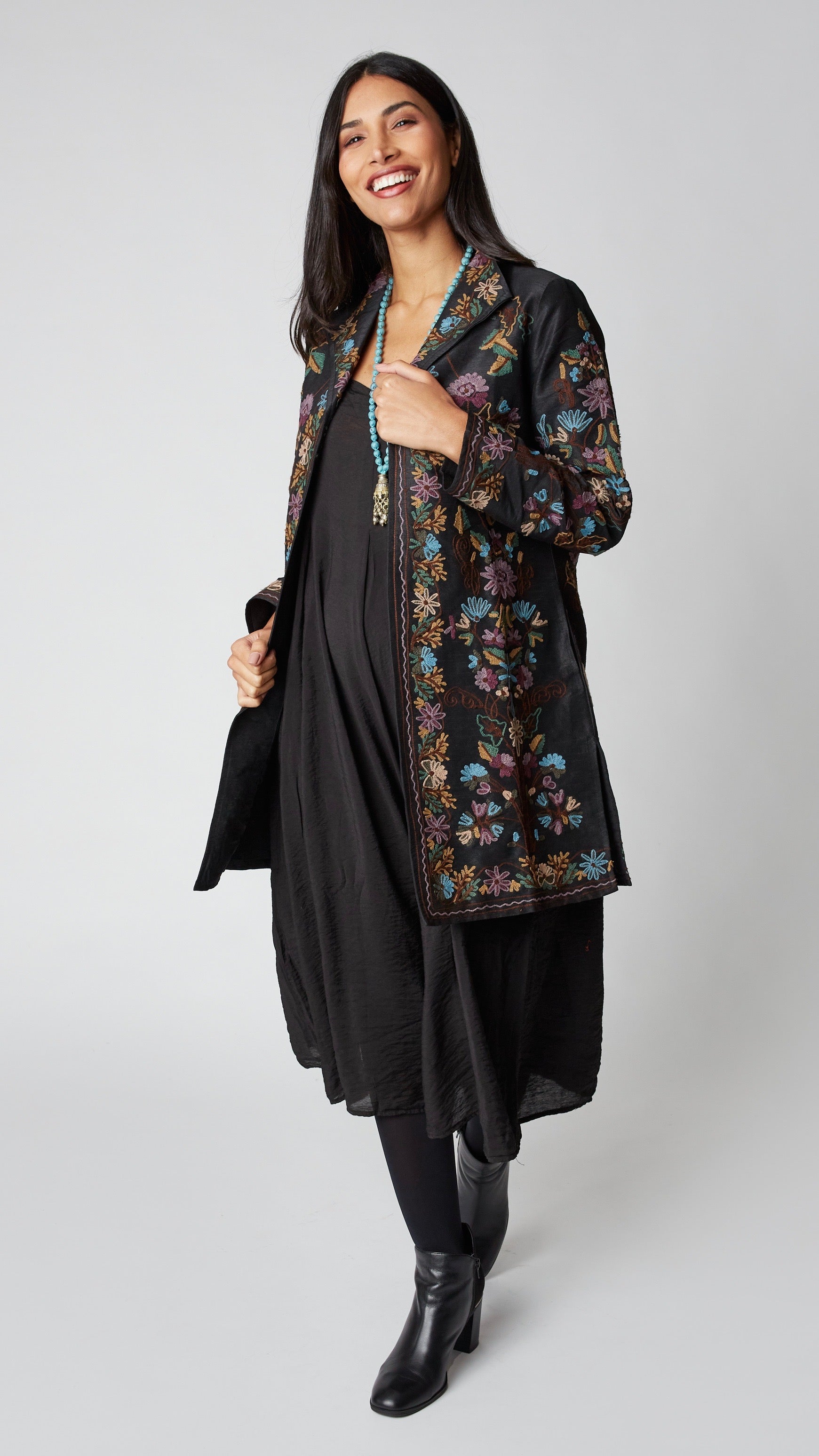 Model wearing black silk duster embroidered in dusty blue, purple, and brown tones over black rayon romper and black suede boots.