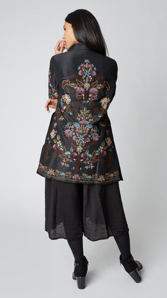 Rearview of model wearing black silk duster embroidered in dusty blue, purple, and brown tones shows intricate embroidery on rear panel.
