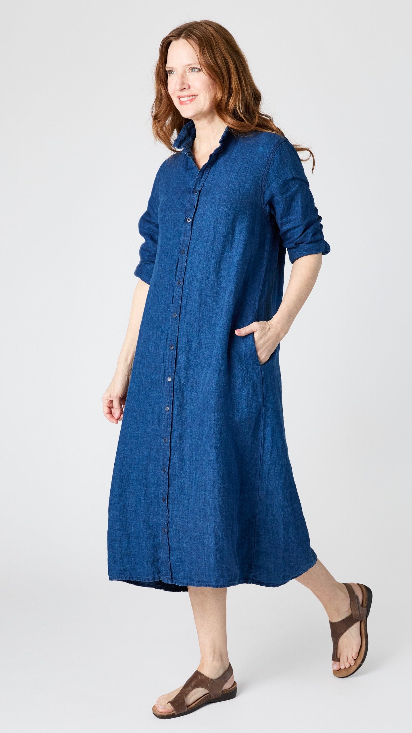Model wearing indigo twill shirtdress with pointed collar and full length button-up panel, and brown leather sandals.