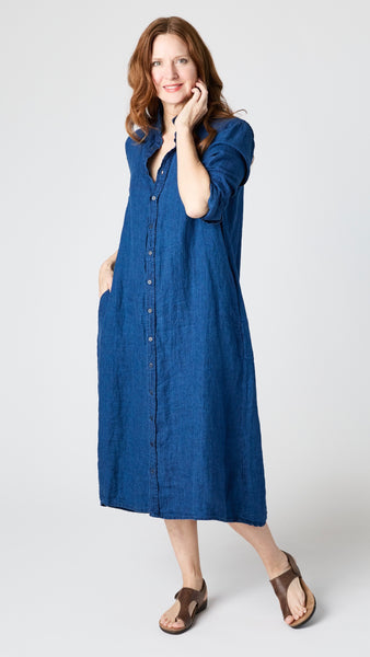 Model wearing indigo twill shirtdress with pointed collar and full length button-up panel, and brown leather sandals.