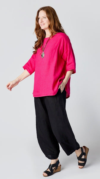 Model wearing "lantana" linen boatneck top with 3/4 sleeves and generous hemline, with black linen lantern pants, and black leather sandals.