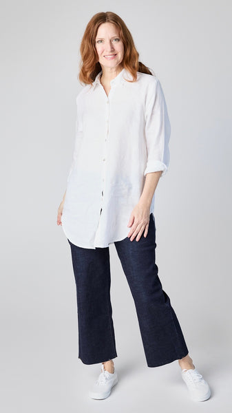 Model wearing white linen button-up shirt with collar and handkerchief hem with indigo cropped wideleg jeans and white sneakers..
