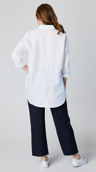 Model wearing white linen button-up shirt with collar and handkerchief hem with indigo cropped wideleg jeans and white sneakers.