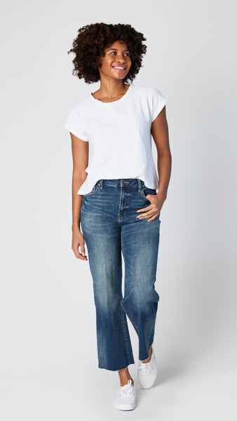 Model wearing white cotton-linen jersey top with cropped sleeves, boatneck, and boxy silhouette with cropped wide-leg dark vintage wash jeans, and white sneakers..