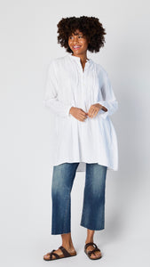 Model wearing white cotton twill tunic with front button, long sleeves, pleating at yoke, and cropped wideleg midwash jeans..