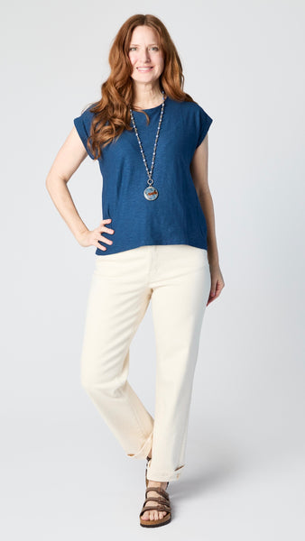 Model wearing ink cotton-linen jersey top with cropped sleeves, boatneck, and boxy silhouette with ecru straight leg jeans and brown sandals.