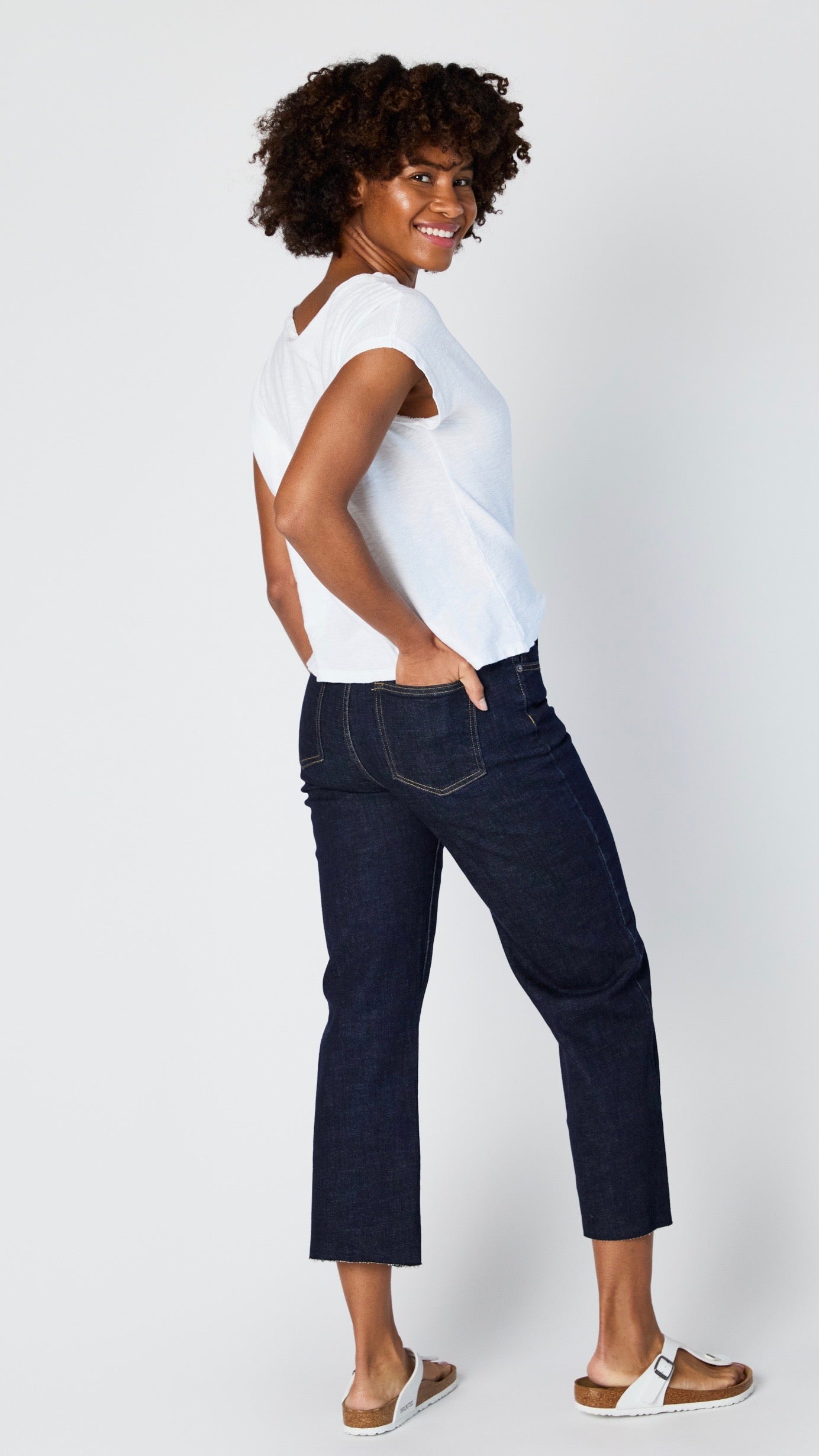 Model wearing dark-wash cropped wide leg jeans with raw hem, white cotton/jersey blend short sleeve tee, and white sandals. 