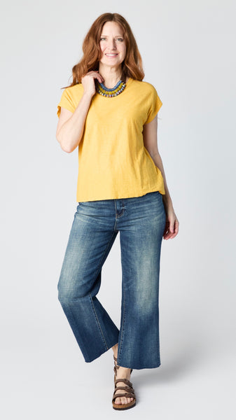 Model wearing sunflower cotton-linen jersey top with cropped sleeves, boatneck, and boxy silhouette with cropped dark wash wide-leg jeans and brown sandals.