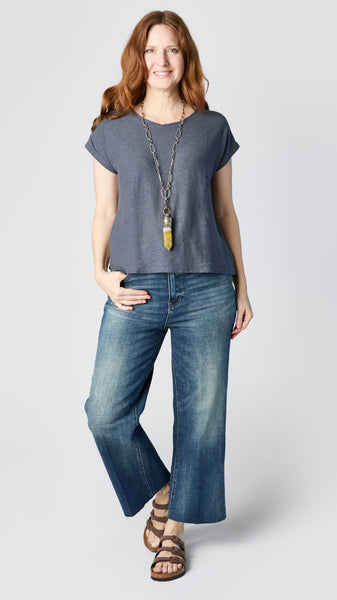 Model wearing anthracite cotton-linen jersey top with cropped sleeves, boatneck, and boxy silhouette with cropped wide-leg dark vintage wash jeans, and brown leather sandals.