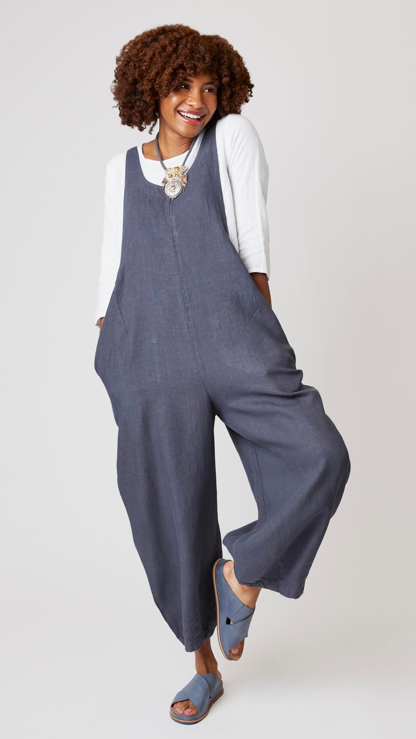Model wearing "iron" linen overall jumpsuit with wide cropped dart leg, white 3/4 sleeve bias cut tee, and gray suede sandals.