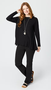 Model wearing black long sleeve swing top, black bootcut denim jeans, silver pendant necklace, and black leather sandals.