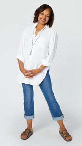 Model wearing white double cotton button-up tunic top with front pocket and shirttail hem, midwash boyfriend jeans, and brown leather sandals.