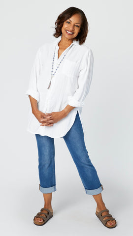 Model wearing white double cotton button-up tunic top with front pocket and shirttail hem, midwash boyfriend jeans, and brown leather sandals.