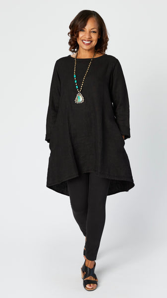 Model wearing black high-low linen tunic with long sleeves, silver beaded turquoise pendant necklace,  black cotton leggings, and black leather sandals.