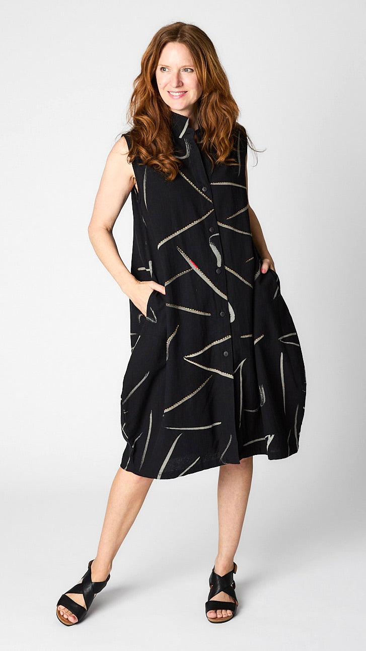 Model wearing black & white front button-opening sleeveless dress/vest with bubble silhouette and raised collar, and black leather sandals. 