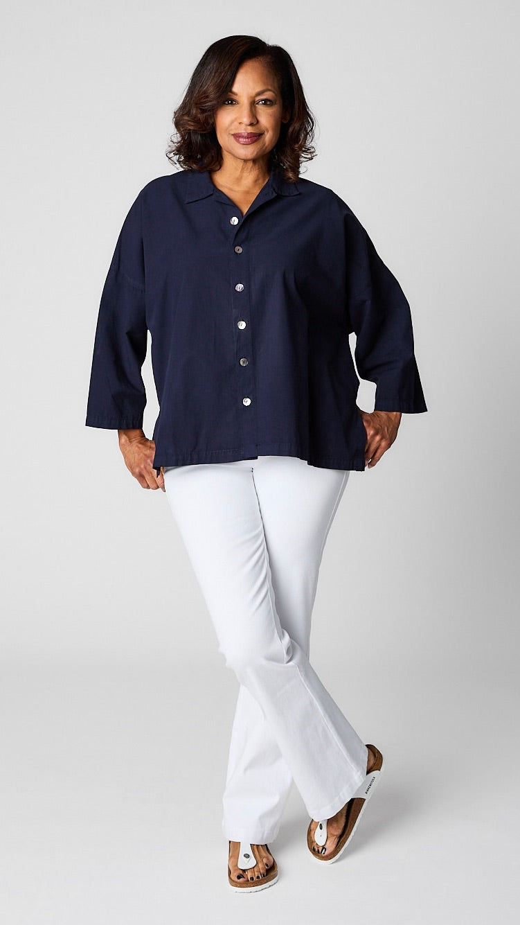 Model wearing indigo button-up top with relaxed hemline and 3/4 sleeves over white bootcut jeans and white sandals.