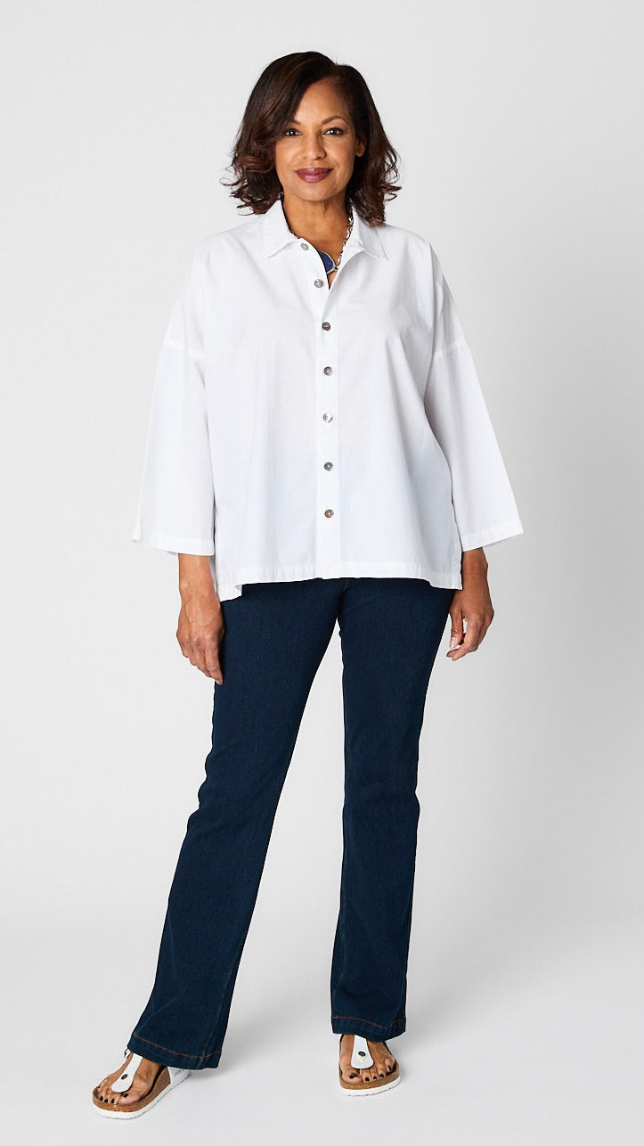 Model wearing "chalk" white button-up top with relaxed hemline and 3/4 sleeves over indigo baby bootcut jeans and white sandals.