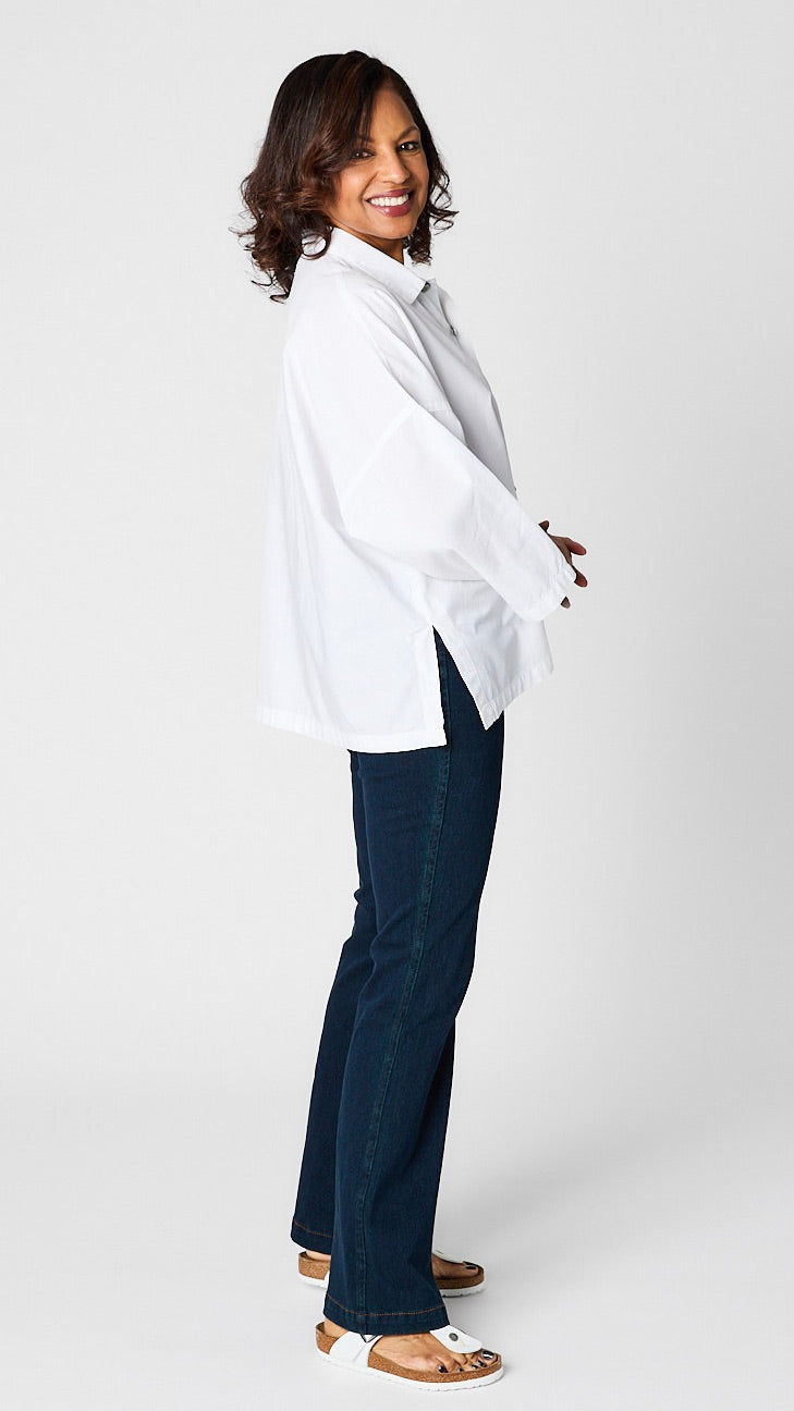 Model wearing "chalk" white button-up top with relaxed hemline and 3/4 sleeves over indigo baby bootcut jeans and white sandals.