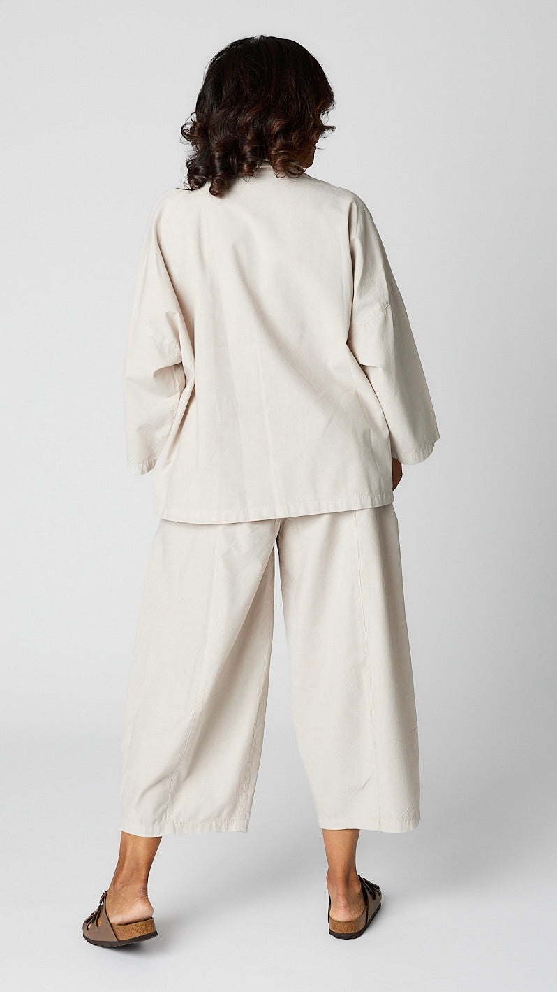 Model wearing cloud button-up top with relaxed hemline and 3/4 sleeves over cloud cropped one pocket pants and brown sandals.