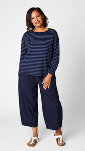 Model wearing "indigo" striped relaxed long sleeve tee, "indigo" cropped pant with one pocket, and white leather sandals.