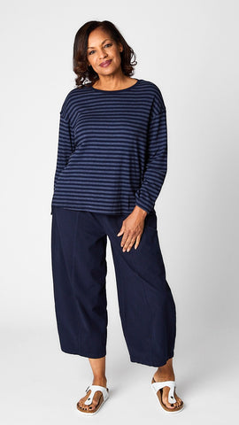 Model wearing "indigo" striped relaxed long sleeve tee, "indigo" cropped pant with one pocket, and white leather sandals.