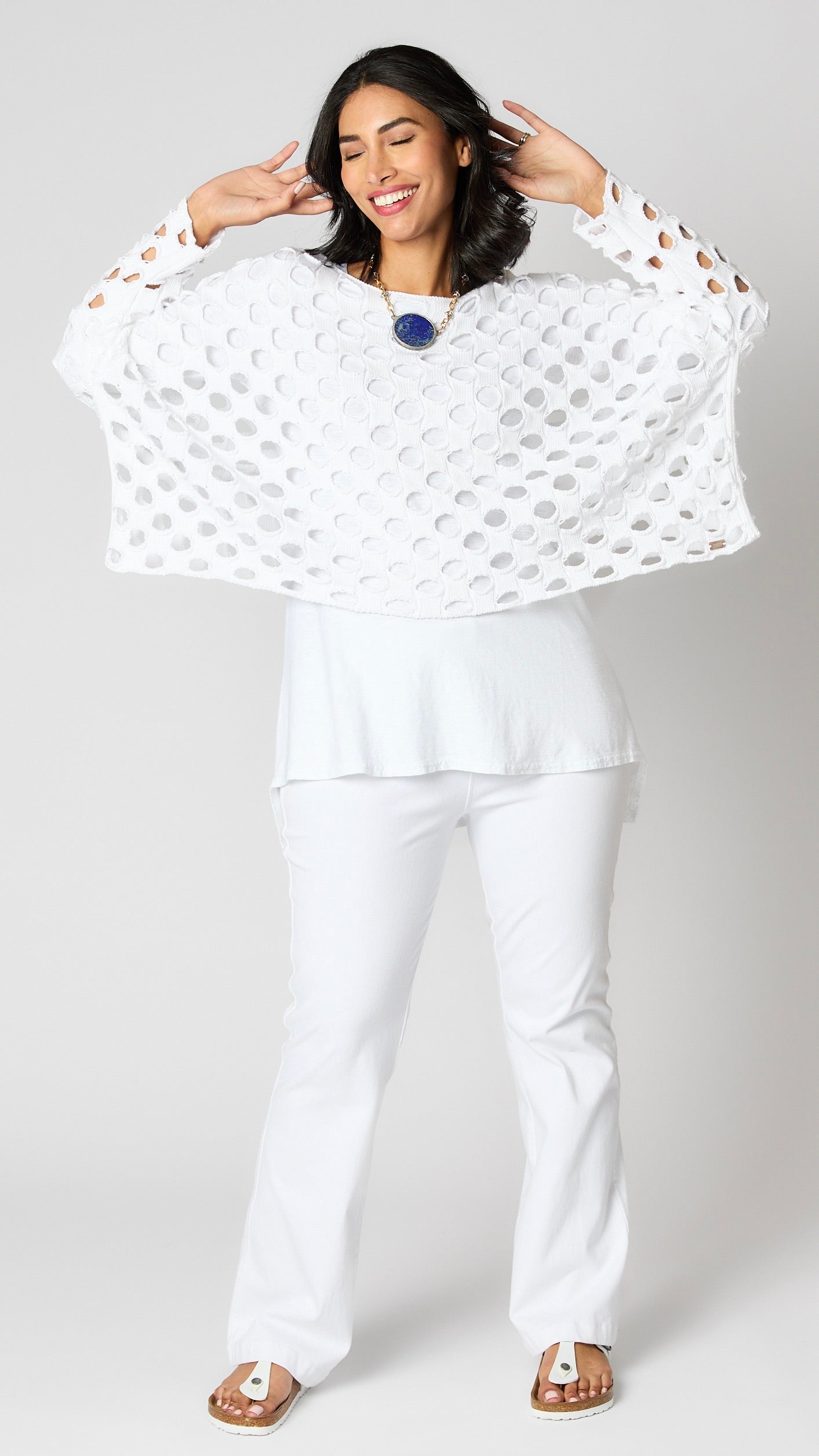 Model wearing white cotton handknit sweater overlay, white cotton-linen blend tunic, and white bootcut jeans.