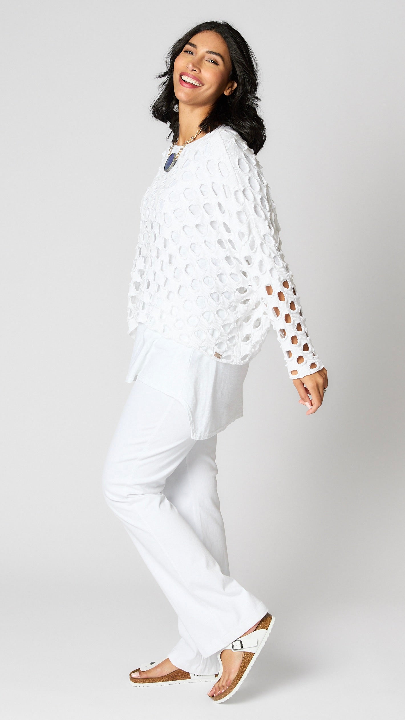 Model wearing white cotton handknit sweater overlay, white cotton-linen blend tunic, and white bootcut jeans.
