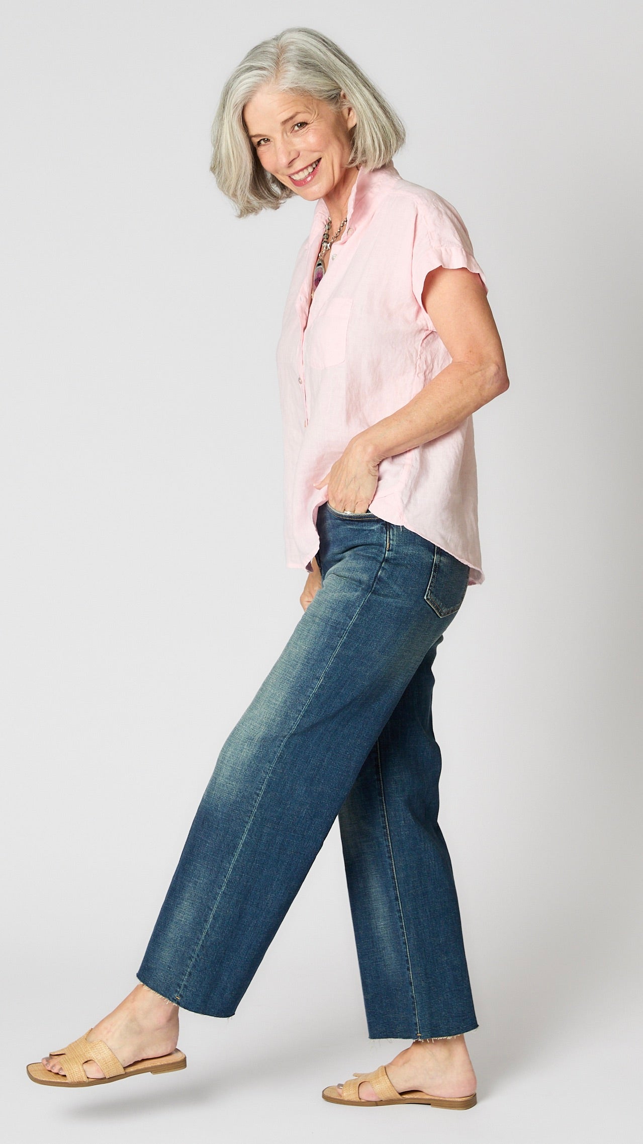 Model wearing pink linen short sleeve button-up shirt, vintage wash cropped jeans, and beige sandals.