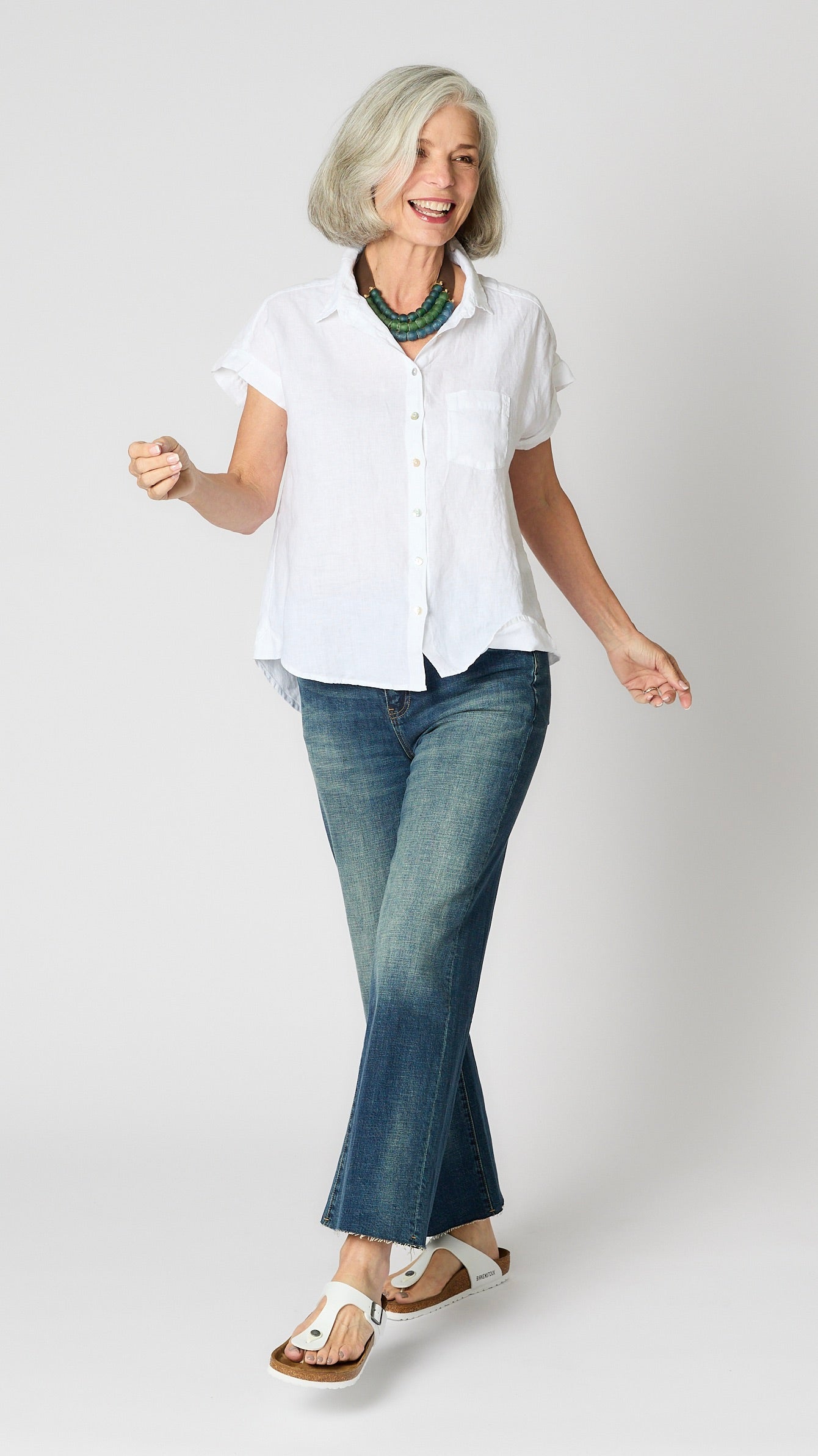 Model wearing white linen short sleeve button-up top, croppped vintage wash jeans, and white sandals. 