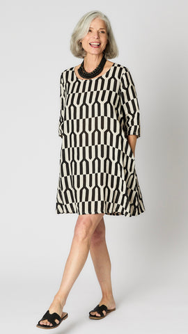 Model wearing tapioca geometric linen dress with 3/4 sleeves, slightly flared body, side seam pockets and knee length hemline. 