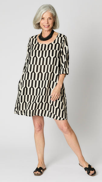 Model wearing tapioca geometric linen dress with 3/4 sleeves, slightly flared body, side seam pockets and knee length hemline.