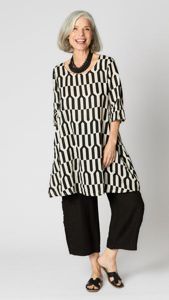 Model wearing tapioca geometric linen dress with 3/4 sleeves, slightly flared body, side seam pockets and knee length hemline.