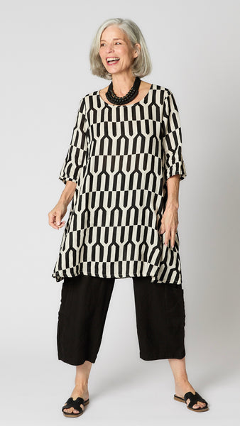 Model wearing tapioca geometric linen dress with 3/4 sleeves, slightly flared body, side seam pockets and knee length hemline.