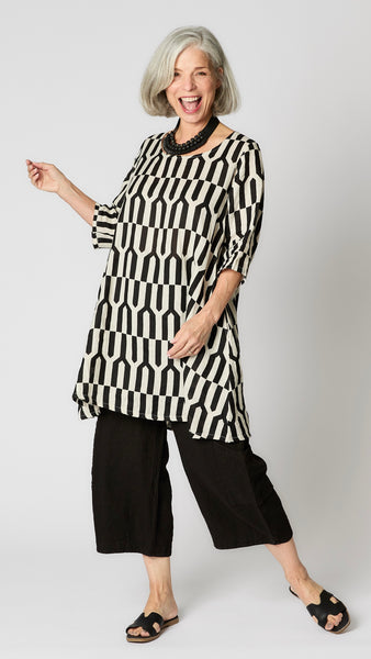 Model wearing tapioca geometric linen dress with 3/4 sleeves, slightly flared body, side seam pockets and knee length hemline.