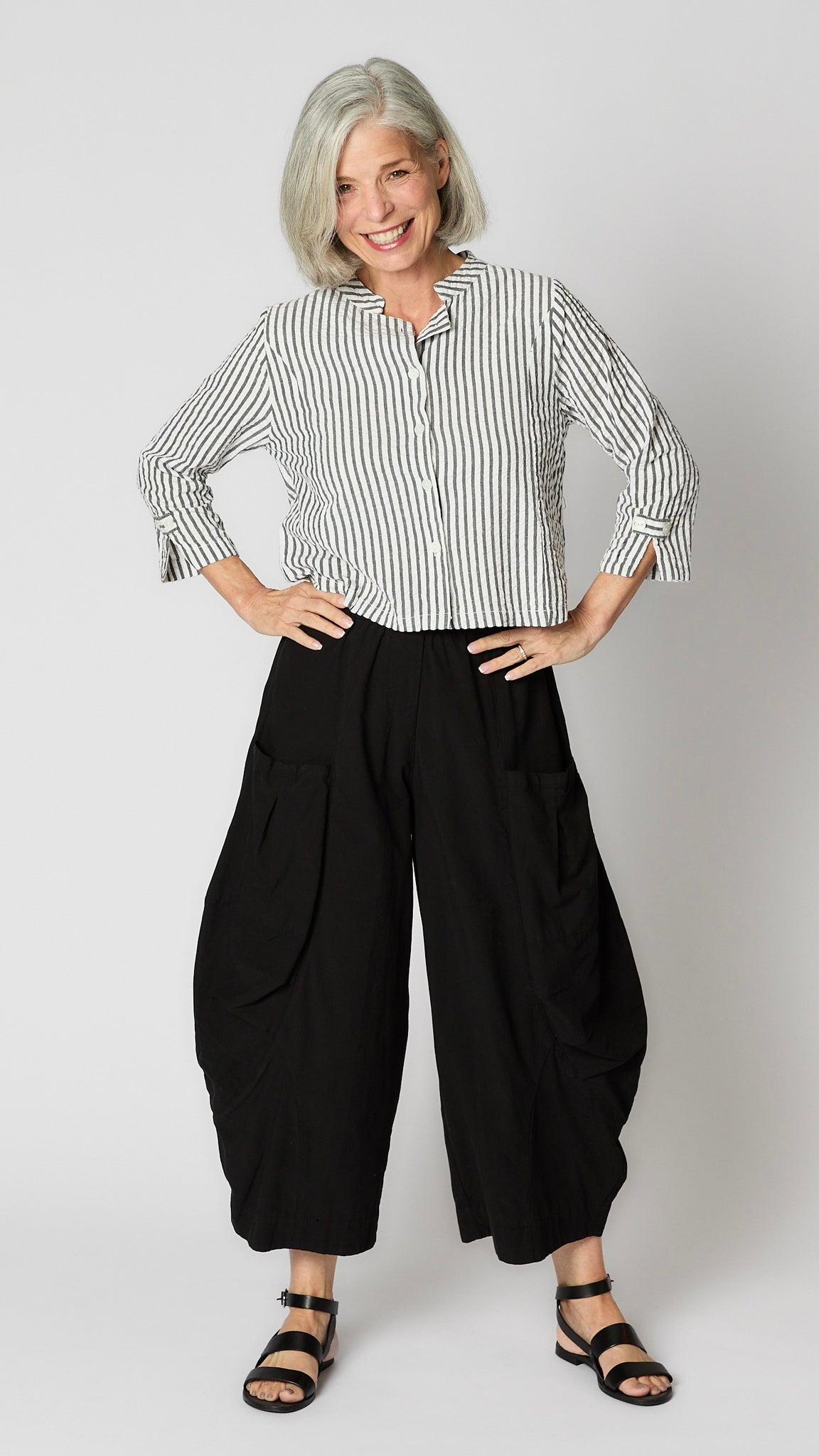 Model wearing short black and white seersucker jacket with Nehru collar, princess seams, and back tab details, black double pocket rayon pants, and black sandals.