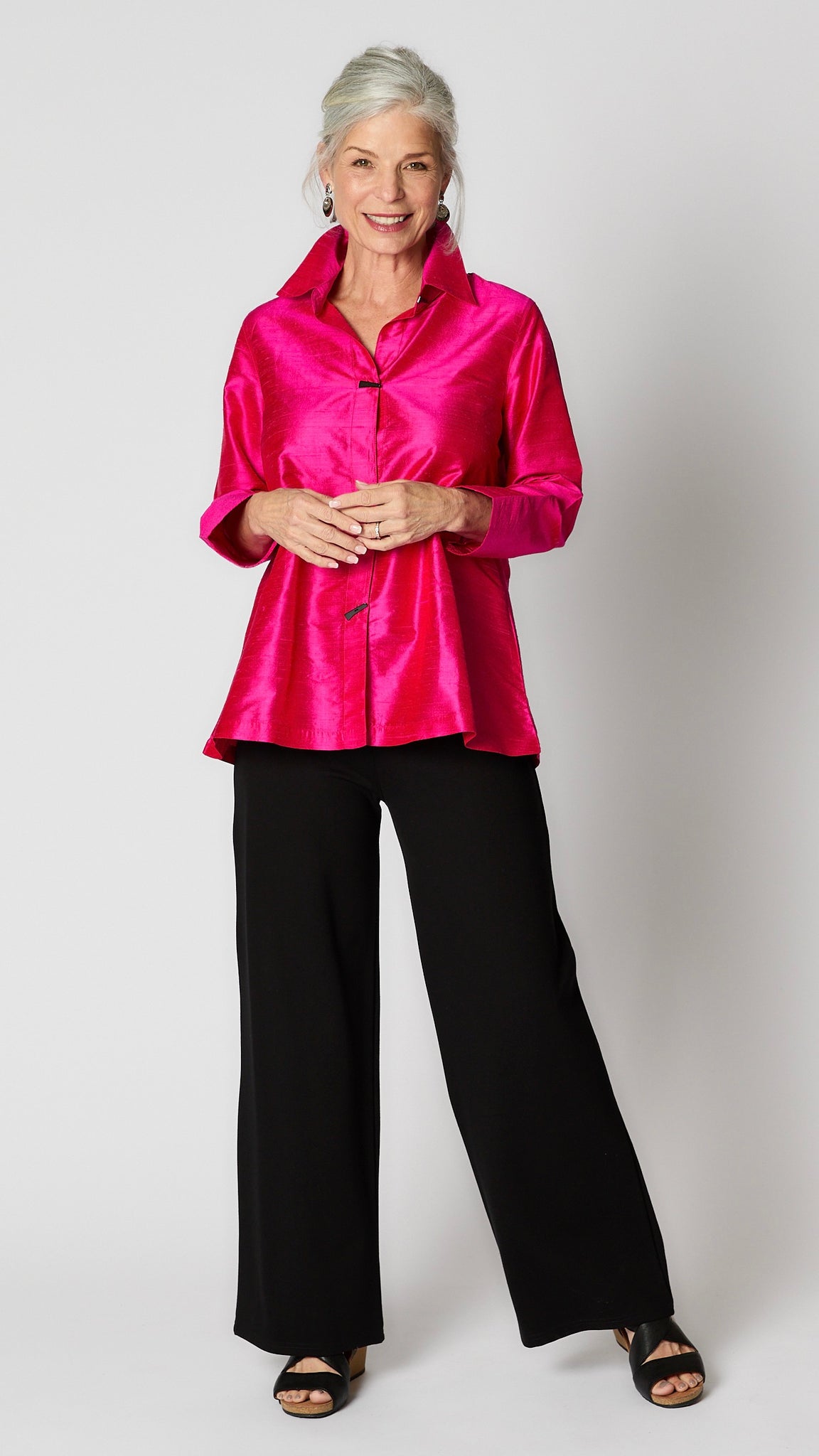 Model wearing fuchsia raw silk button-up blouse with black horn buttons and 3/4 sleeves, black wideleg trousers, and black wedge sandals.  