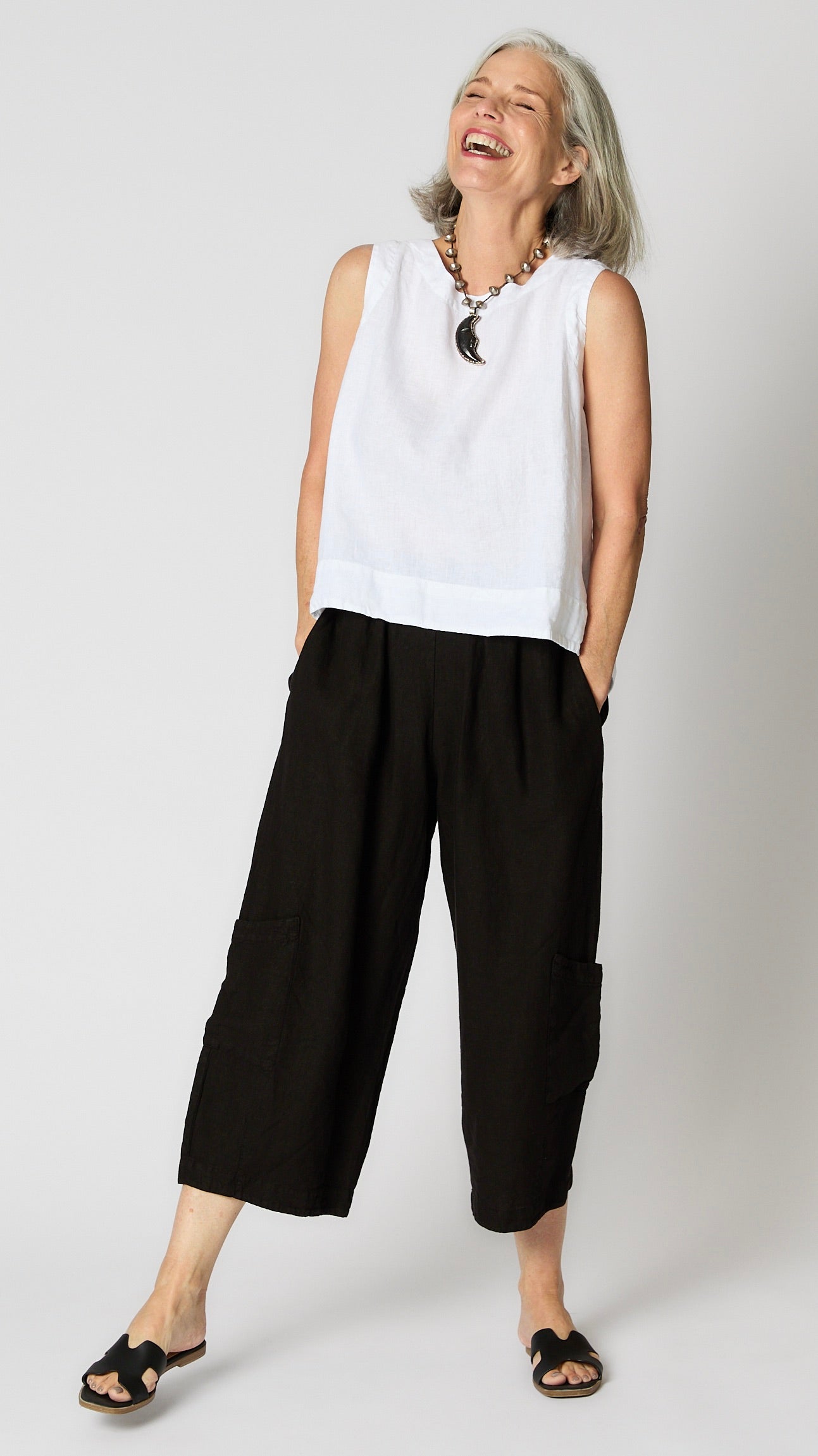 Model wearing white linen sleeveless tank with hi-lo silhouette, and black cropped linen pants with patch pockets.  