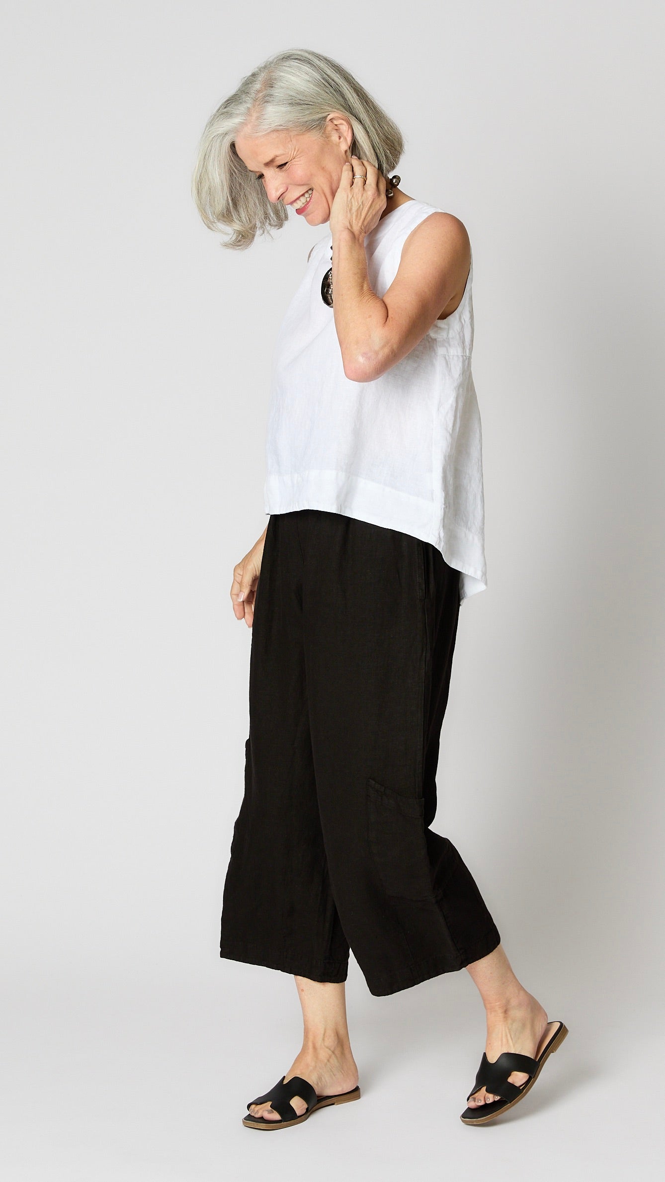Model wearing white linen sleeveless tank with hi-lo silhouette, and black cropped linen pants with patch pockets.  