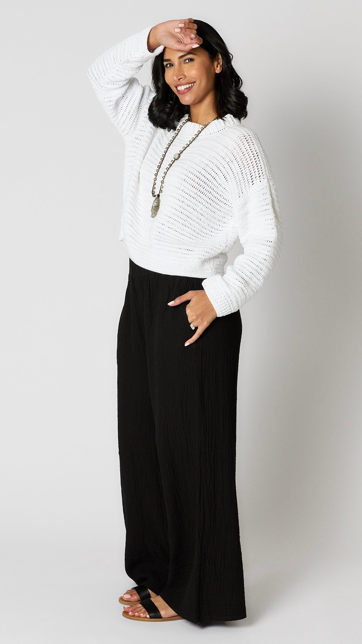 Model wearing black crinkle cotton palazzo, highwaisted pant, white crochet cotton sweater with cropped hemline, and black leather sandals.