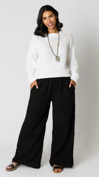 Model wearing black crinkle cotton palazzo, highwaisted pant, white crochet cotton sweater with cropped hemline, and black leather sandals.