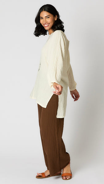 Model wearing chocolate crinkle cotton palazzo pants, cream oversized hi-lo double cotton tunic, and brown leather sandals. 