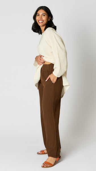 Model wearing chocolate crinkle cotton palazzo pants, cream oversized hi-lo double cotton tunic, and brown leather sandals. 