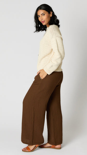 Model wearing chocolate crinkle cotton palazzo pants, cream hand crocheted cropped sweater, and brown leather sandals.