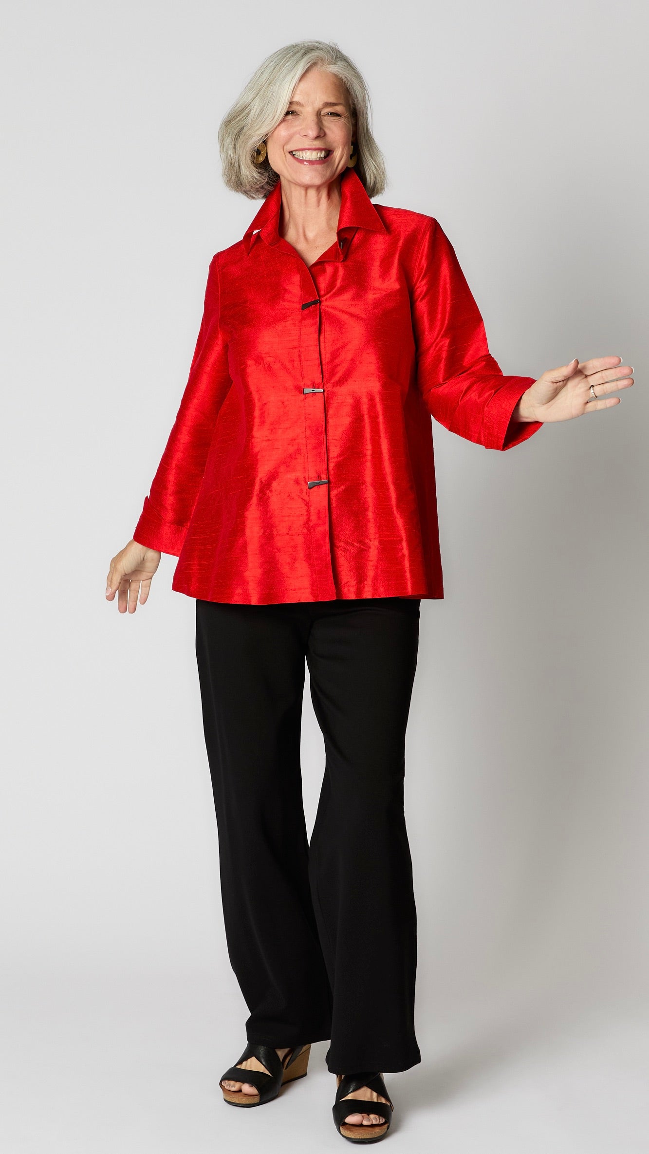 Model wearing red raw silk button-up blouse with black horn buttons and 3/4 sleeves, black wideleg trousers, and black wedge sandals.  